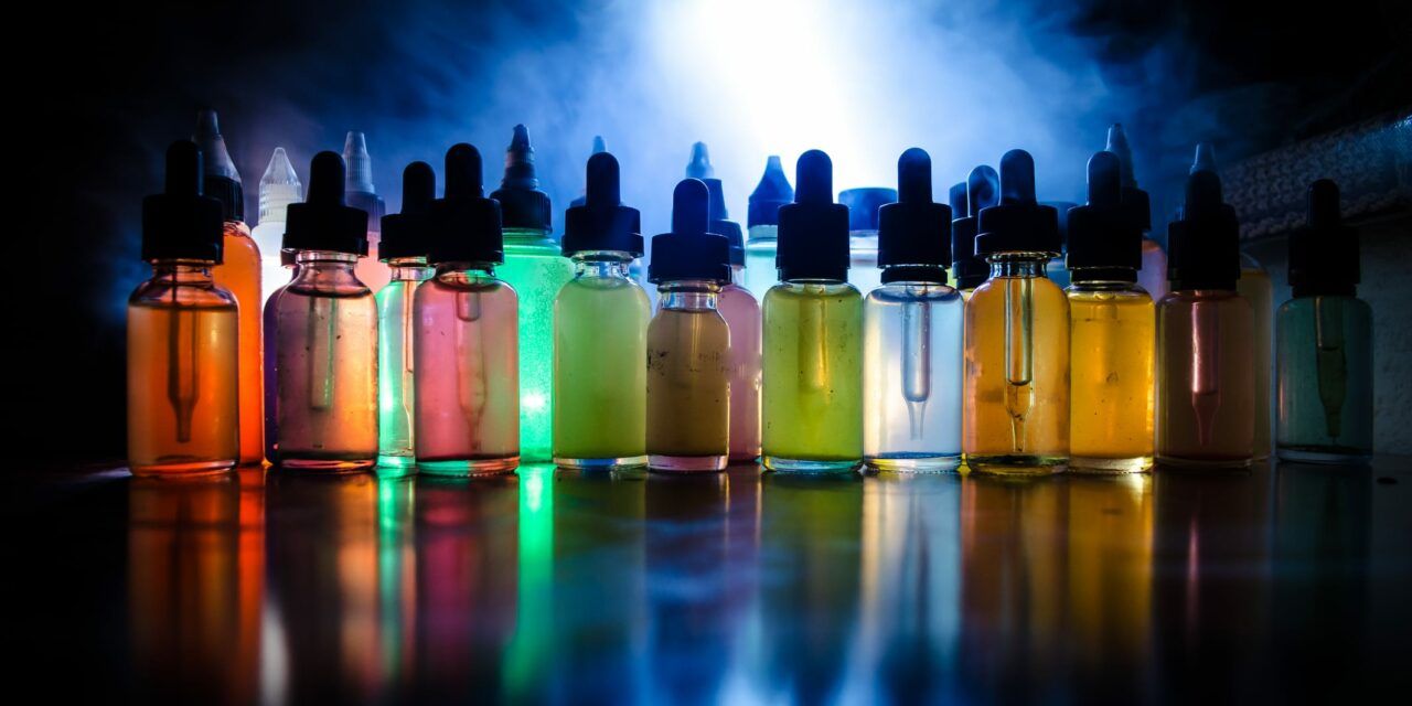 A row of e-liquid dropper bottles in assorted colours, lit from behind.