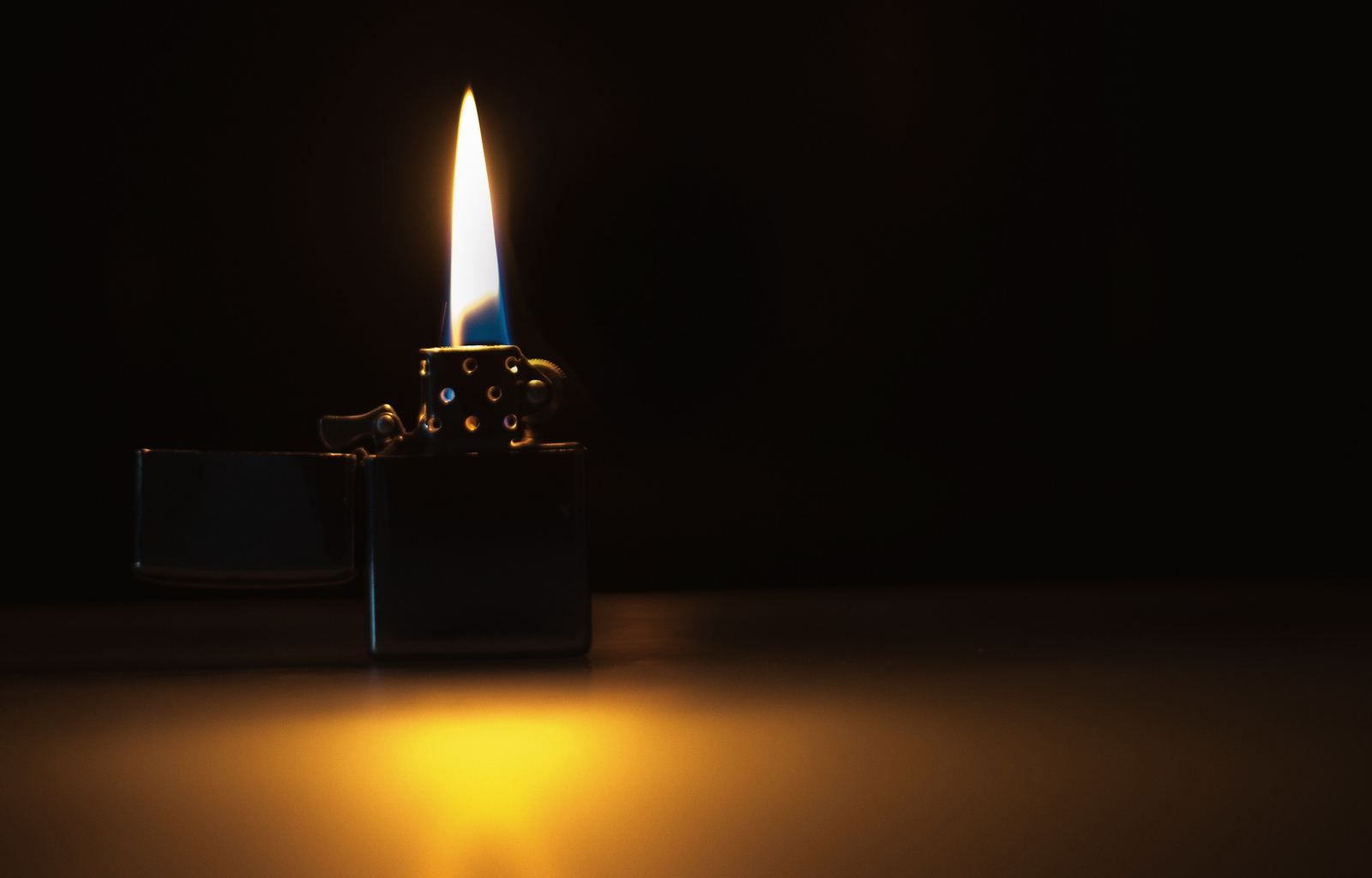 A lit flip-top lighter burning against a dark background.