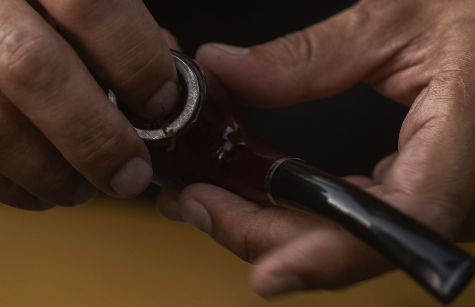 Hands packing tobacco into the bowl of a briar pipe.
