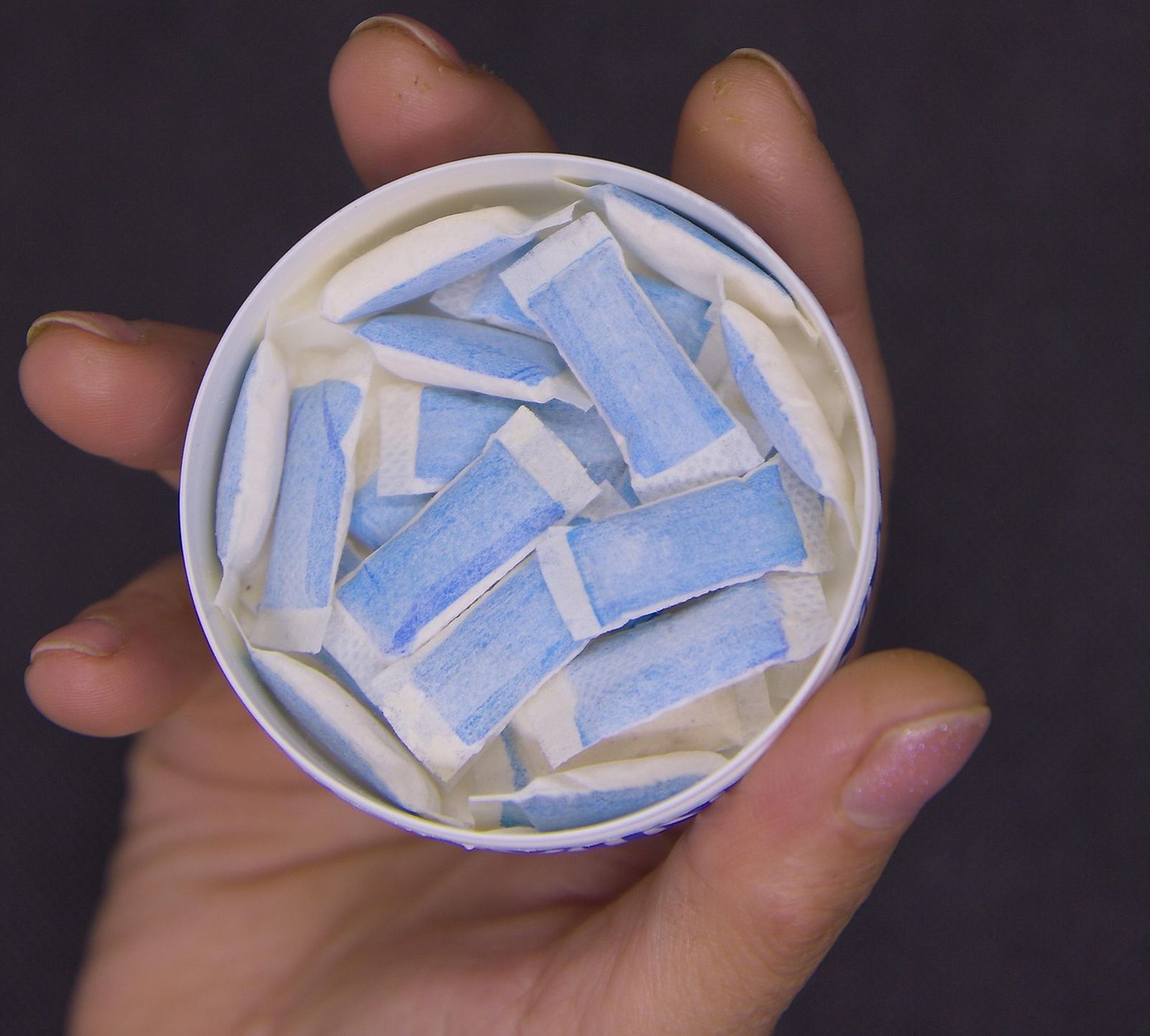 An open tin of nicotine pouches held in one hand.
