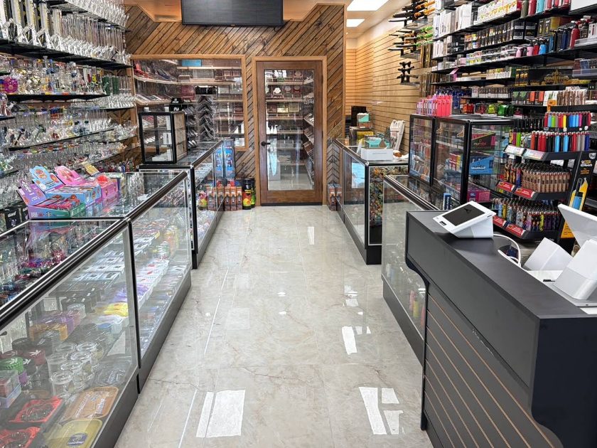 The shop floor looking toward the back: glass display cases down both sides, the counter on the right, and the cedar-lined walk-in humidor at the end.