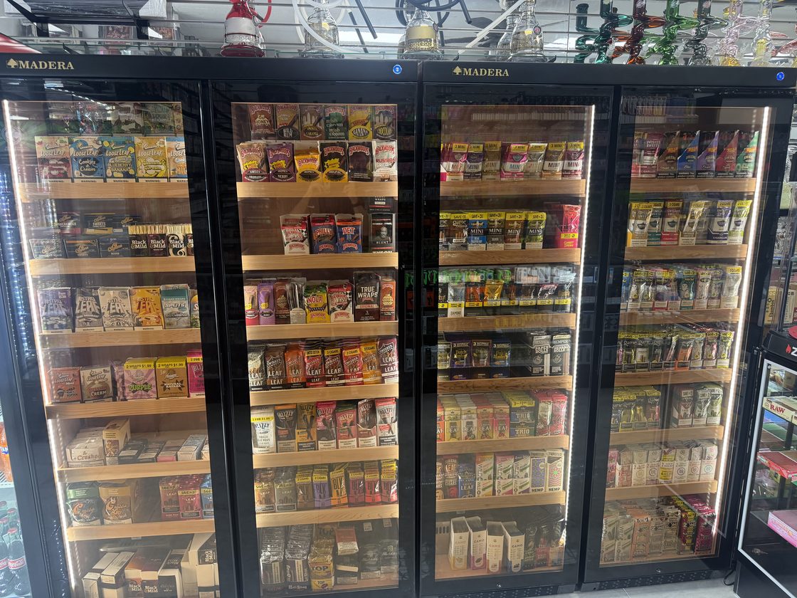 Four glass-door cabinets with cedar shelving, filled with blunt wraps, cigarillos and leaf, with glass water pipes on the shelf above them.